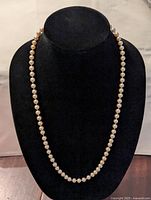 Full length view of the long faux pearl necklace displayed on a black mannequin stand, showing the entire continuous strand of pearls.