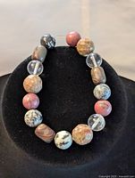 Photo showing multistone bracelet on black display, featuring round and faceted beads in various colors and patterns.