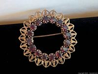 Front view showing circular wreath with 16 deep red faceted stones in openwork gold heart motifs