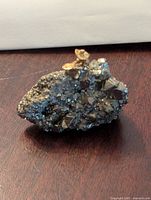 Front angled view of a gold-colored prospector figurine sitting on a cluster of shiny pyrite crystals on a dark wooden surface.