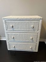 Front view of white wicker dresser with 3 drawers showing woven wicker design and round knob handles.