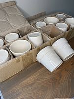 Set of 12 beige glazed ceramic plant pots in cardboard packaging, some removed to show shape and size.