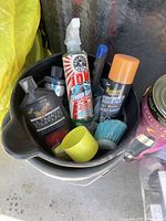 View of bucket containing various car wash and cleaning products including Chemical Guys compound, spray bottles, brushes, and containers.