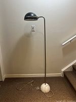 Full view of black metal floor lamp with dome shade, curved arm, spherical white marble base, power cord visible on floor.