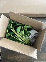 Open cardboard box showing stems and green artificial leaves wrapped in protective bubble wrap and packed inside the box.