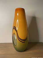 Front view of the hand-blown glass vase showing the orange to green gradient, black swirl, and clear glass features.