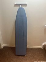 Ironing board standing upright against wall showing full height and blue fabric cover