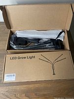 Two brown cardboard boxes labeled 'LED Grow Light' containing LED grow lights with four flexible gooseneck heads, power cords, and instruction manuals, in unopened packaging.