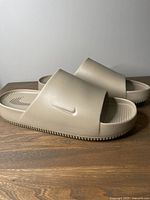 Side-by-side view of the beige Nike Calm Slides showing the full length rubber outsole and wide strap with the Nike swoosh logo.