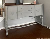 Front view showing rustic gray painted sideboard with original brown wood top, two doors and two drawers with round chrome knobs.