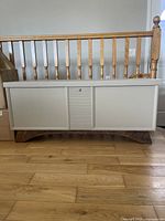 Front view of vintage Lane cedar chest with taupe beige painted finish and walnut stained base, placed near wooden railing.
