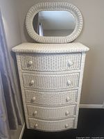 Front view of white wicker dresser with five drawers and matching wicker-framed mirror on top.