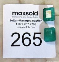 Two rectangular emerald cut green jade gemstones placed on a MaxSold auction label with number 265.