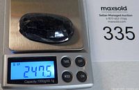 Faceted dark blue sapphire on a digital scale showing weight of 247.5 carats, auction lot number visible.