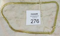 Full length view of gold chain necklace placed flat on a surface with auction tag 276.