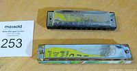 Two vintage harmonicas placed side by side, showing metal covers and hole arrays, with a label indicating auction number 253.