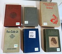 Top-down view of six vintage hardcover books showing titles, dates, and varied cover colors including faded red, beige, gray, blue, and dark green.