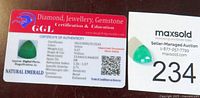 GGL Certificate of Authenticity card showing detailed information and the emerald gemstone placed next to the card and lot tag number 234.