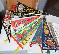 Seven vintage British Columbia pennants laid out on a white surface showing various cities and themes.