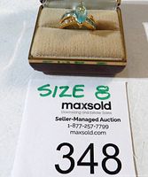 Ring in display box, showing front view with light blue marquise gemstone, and signage indicating size 8.