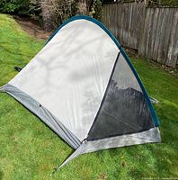 Side view of beige and gray tent body featuring large mesh door panel, set up on grass outdoors.
