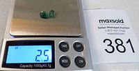 Two faceted green gemstones on a weighing scale displaying total weight 2.5 carats