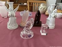 View of all 7 pieces arranged on table, showing two white angel candlestick holders, four different praying hands figurines, and one glass base