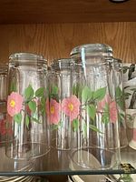 12 clear glass tumblers with pink floral decoration and green leaves, standing upright grouped closely
