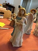 Porcelain angel statue holding a baby, front and side view on a table with other figurines