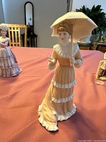 Full view of the porcelain figurine showing the woman with a parasol in a ruffled layered dress.