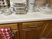 CorningWare dishes stacked and grouped on kitchen counter showing patterns, lids, and different sizes