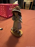 Full view of Tiffany porcelain figurine showing girl in bonnet holding a doll, standing on an oval base.