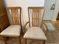 Two wooden chairs with vertical and horizontal slat backs. Seat upholstery is beige with vertical stripes. One chair has armrests, the other does not.