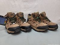 Two pairs of tan and black women's work boots, steel toe, with green and black laces, shown side by side