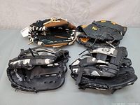 Four baseball gloves shown side by side in one image on grey background.
