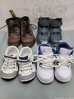 Four pairs of children's shoes including lace-up boots, Puma velcro sneakers, casual shoes, and Jordan sneakers.