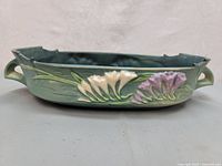 Side view of green Roseville Pottery console bowl showing raised white and purple Freesia flowers and leaf design with handles.