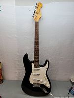 Front view of black Academy electric guitar Strat style with white pickguard and three pickups.