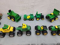 Overview of seven John Deere toy tractors and trucks in green and yellow plastic and metal.