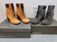 Two pairs of Timberland boots on their respective boxes, tan and grey color, showing side and front profiles.