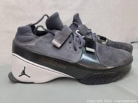 Side view of the right sneaker showing grey suede upper, black strap, and white midsole with Jumpman logo.