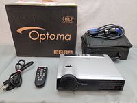 Photo showing the Optoma EP7150 projector with power cable, remote control, VGA cable, carrying case, and original box.