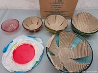 Set of 5 glass bowls in multiple colors with protective cardboard and plastic covers and their lids shown stacked and unpacked