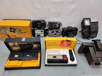 Overview of all cameras and equipment in the lot showing boxed Kodak Pocket Instamatic, Vivitar 600, assorted compact cameras, and Vivitar external flash