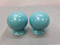 Pair of turquoise blue vintage Fiestaware salt and pepper shakers side by side on a gray surface.