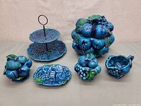 Full view of the six glossy indigo blue ceramic pieces showing fruit motifs and shapes