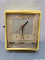 Front view of the yellow Lux electric wall clock showing time and date displays