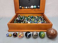 Wide view of marbles in wooden display box with a row of large marbles in front for size comparison.