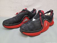 Pair of vintage Nike Air Jordan Trunner LOW LX sneakers displayed showing front and outer sides, black suede upper with red accents and laces.