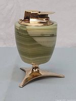 Side view of cylindrical green onyx or marble base with brass tripod stand and lighter mechanism on top.